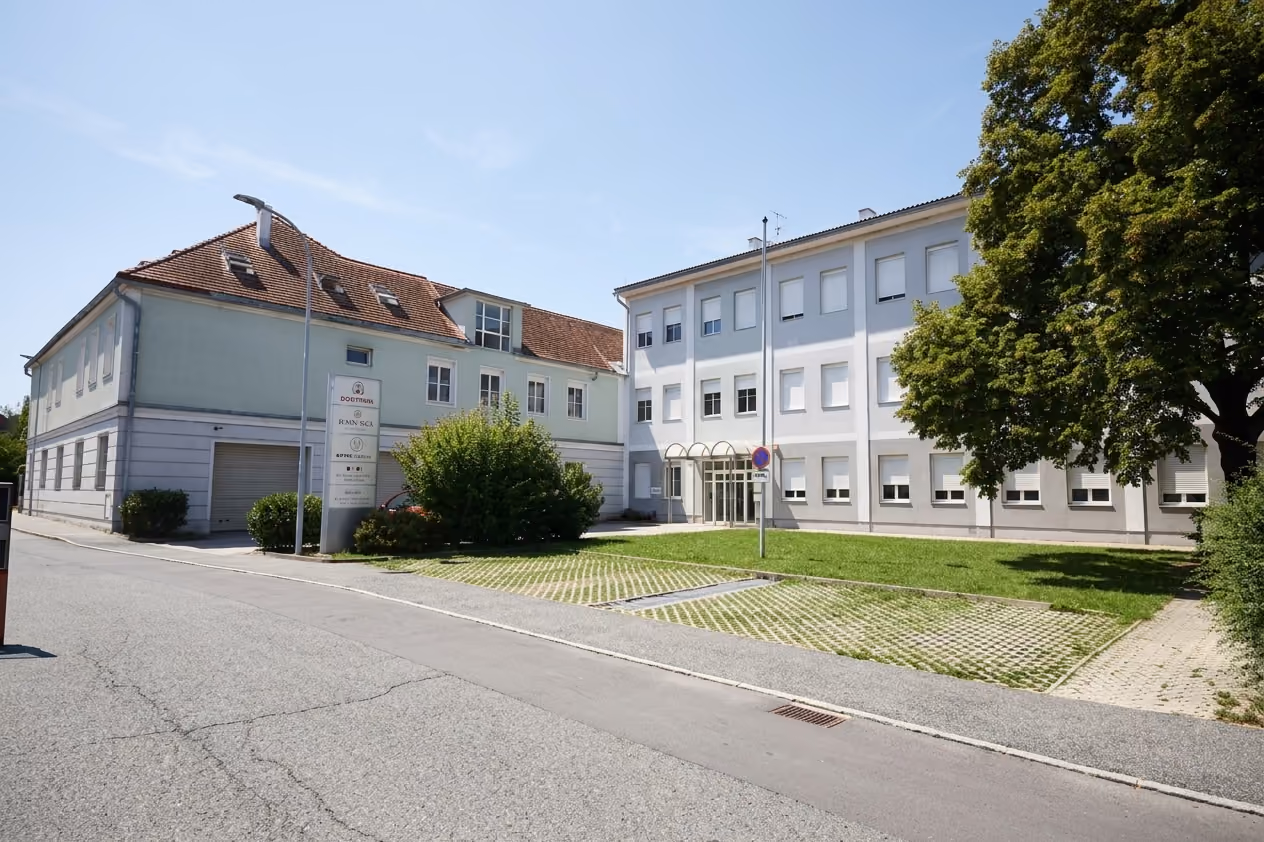 WK8: Gebäudeensemble mit Rasenparkplätzen und großem Baum von der Straße aus